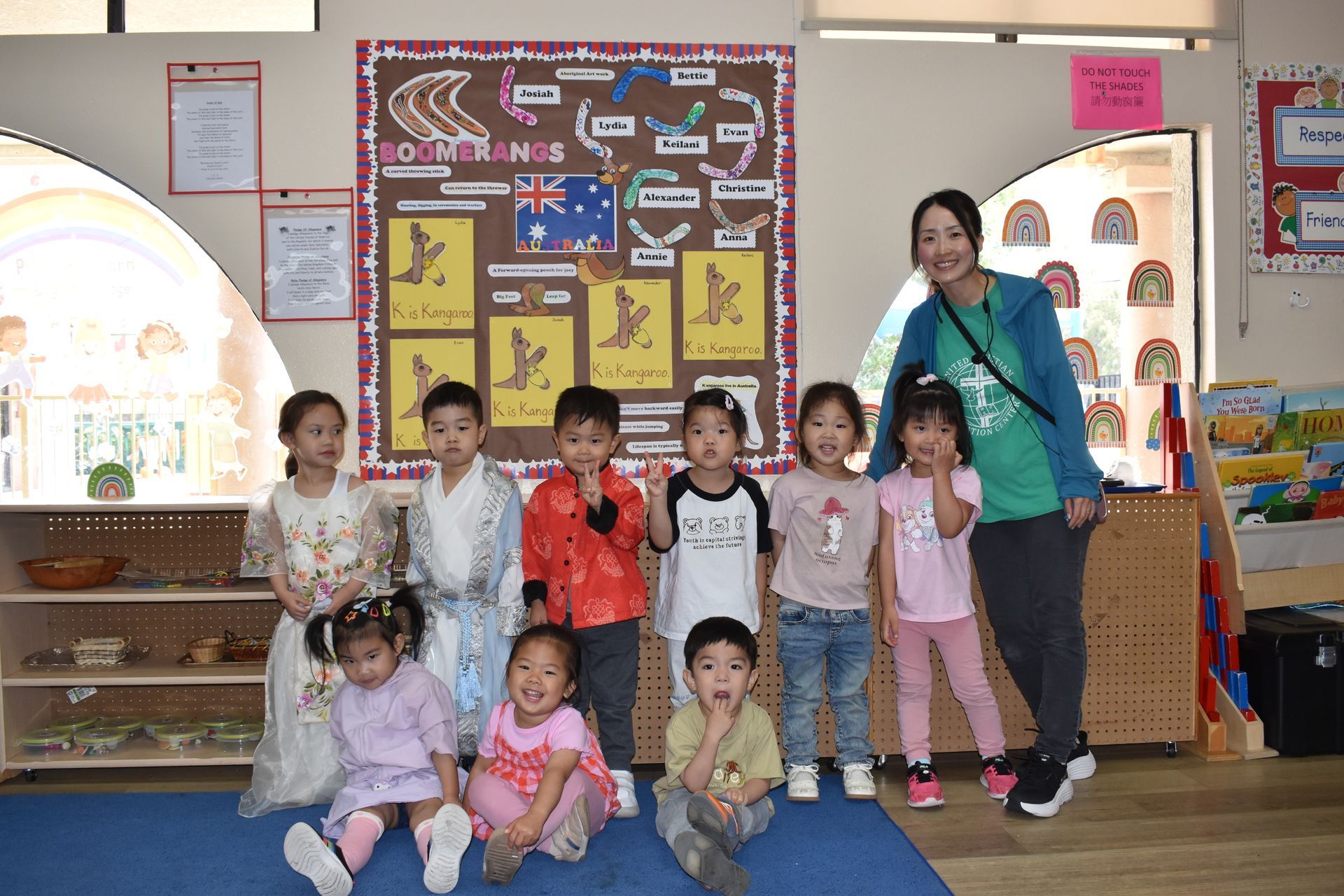 Group of children and an adult teacher pose in a classroom.
