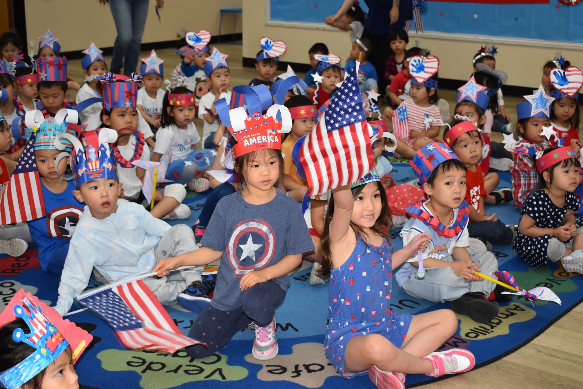Children in red, white, and blue, celebrating with flags and headbands indoors.