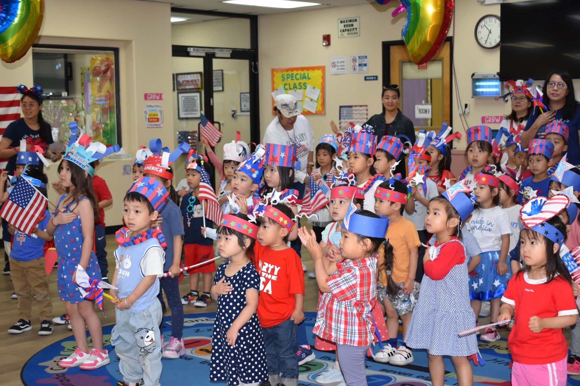 Children in red, white, and blue celebrate with flags and festive headwear in a classroom.