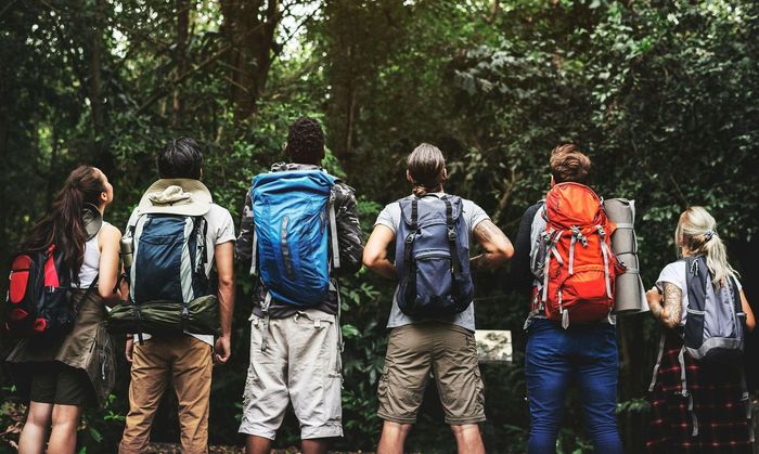 A group of people with backpacks are standing in the woods.