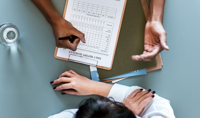 A man and a woman are sitting at a table writing on a clipboard.