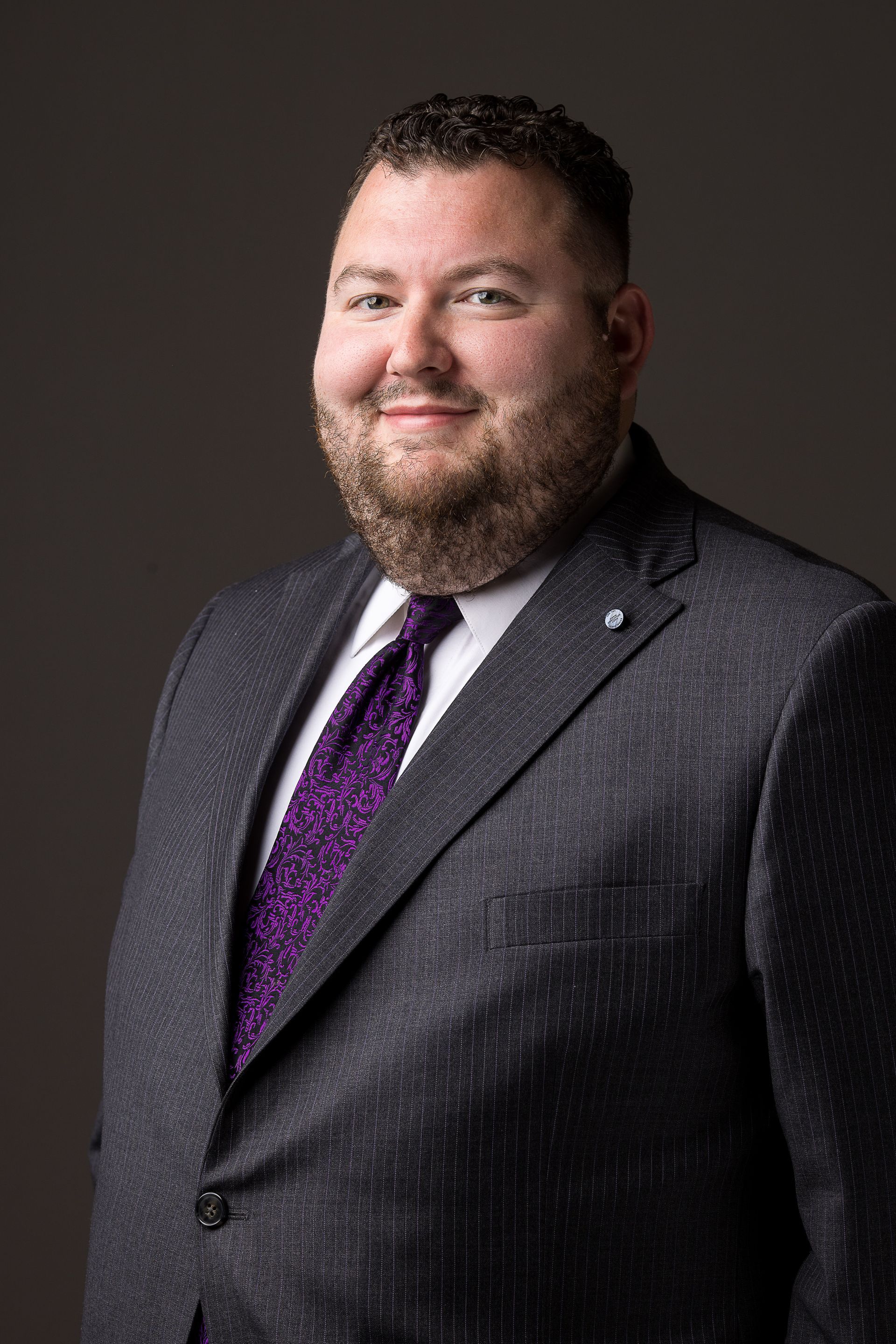Man in suit smiles, close-up headshot with a dark background.