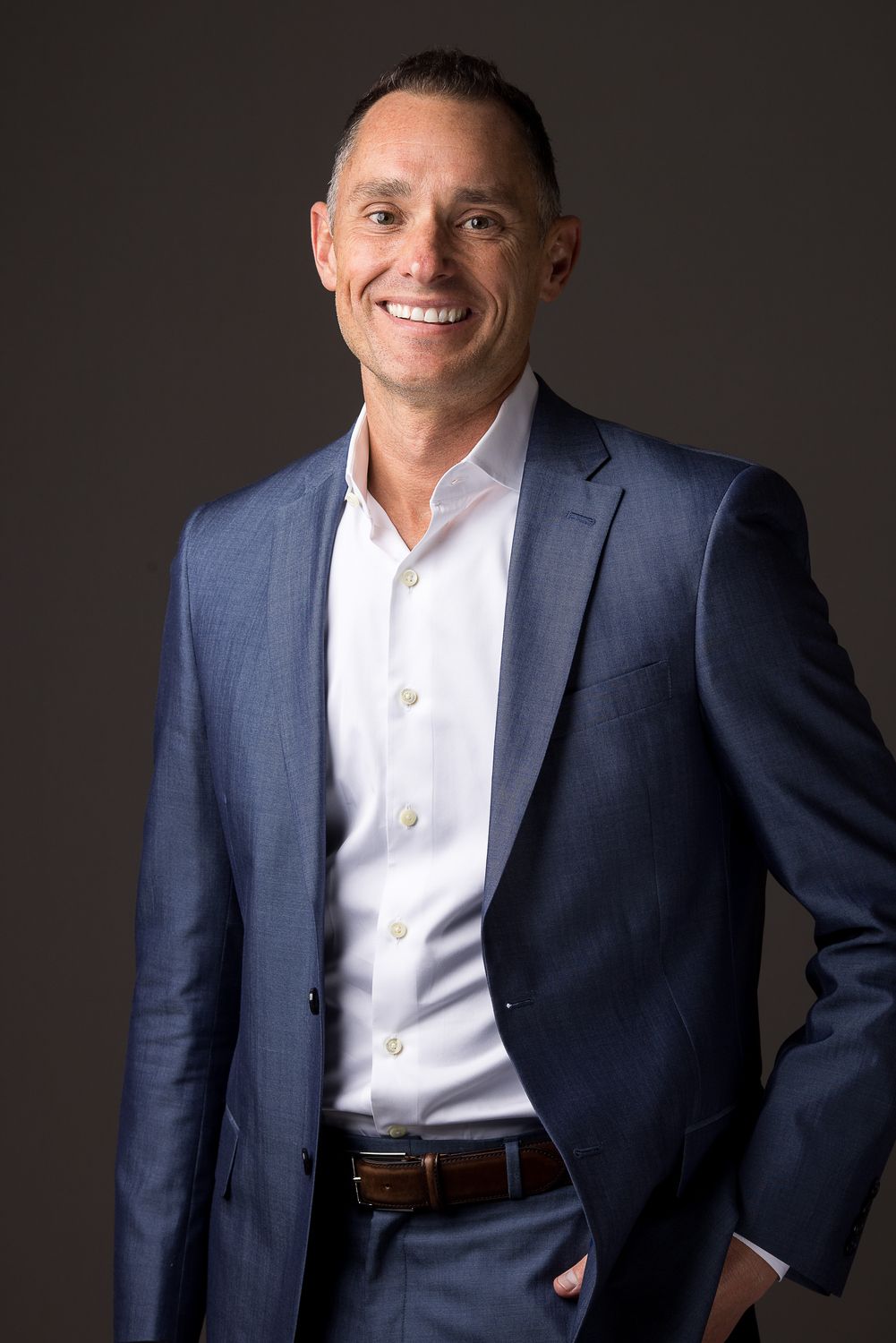 Man in blue suit smiles, dark background.
