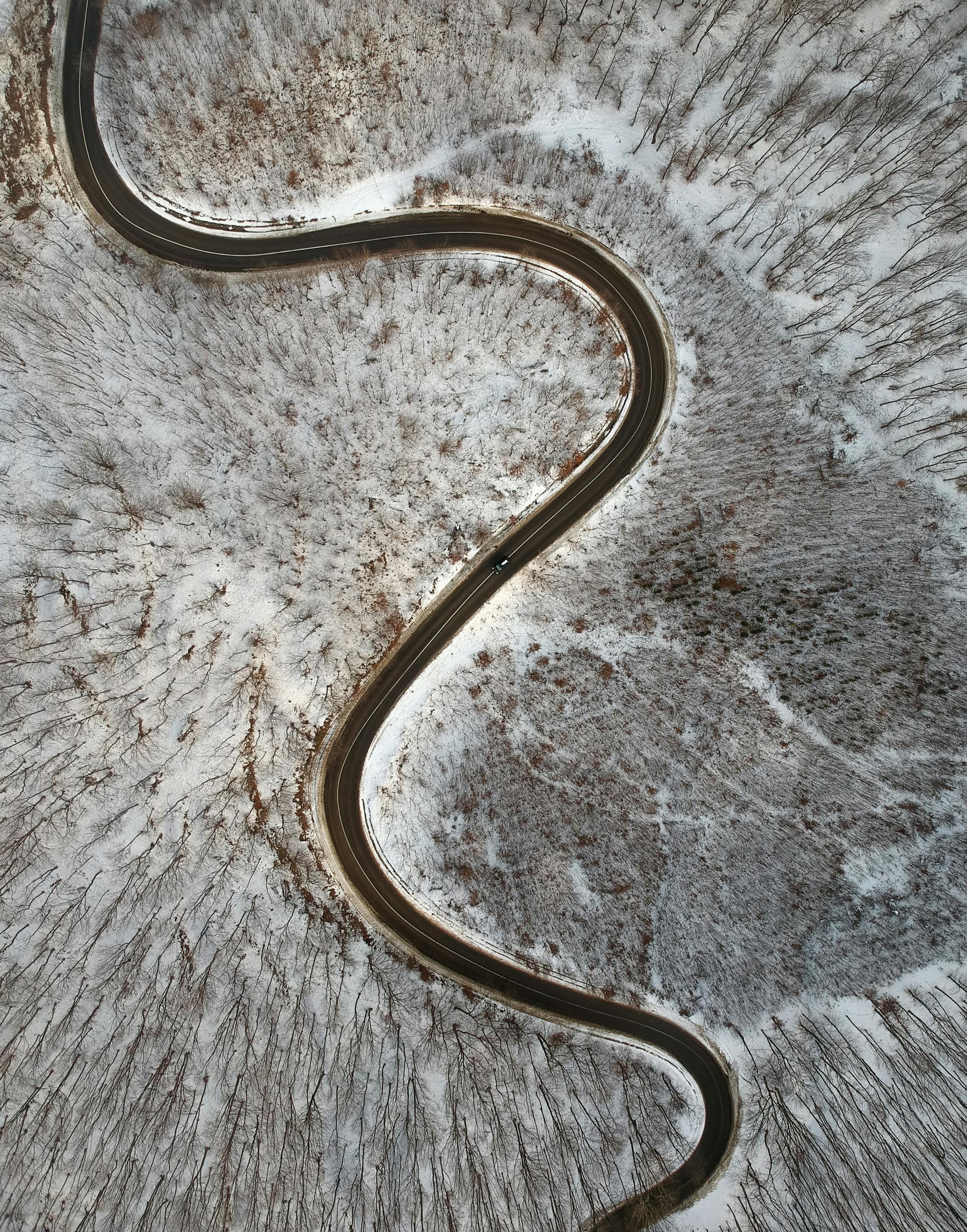Winding road through snow-covered forest, viewed from above.