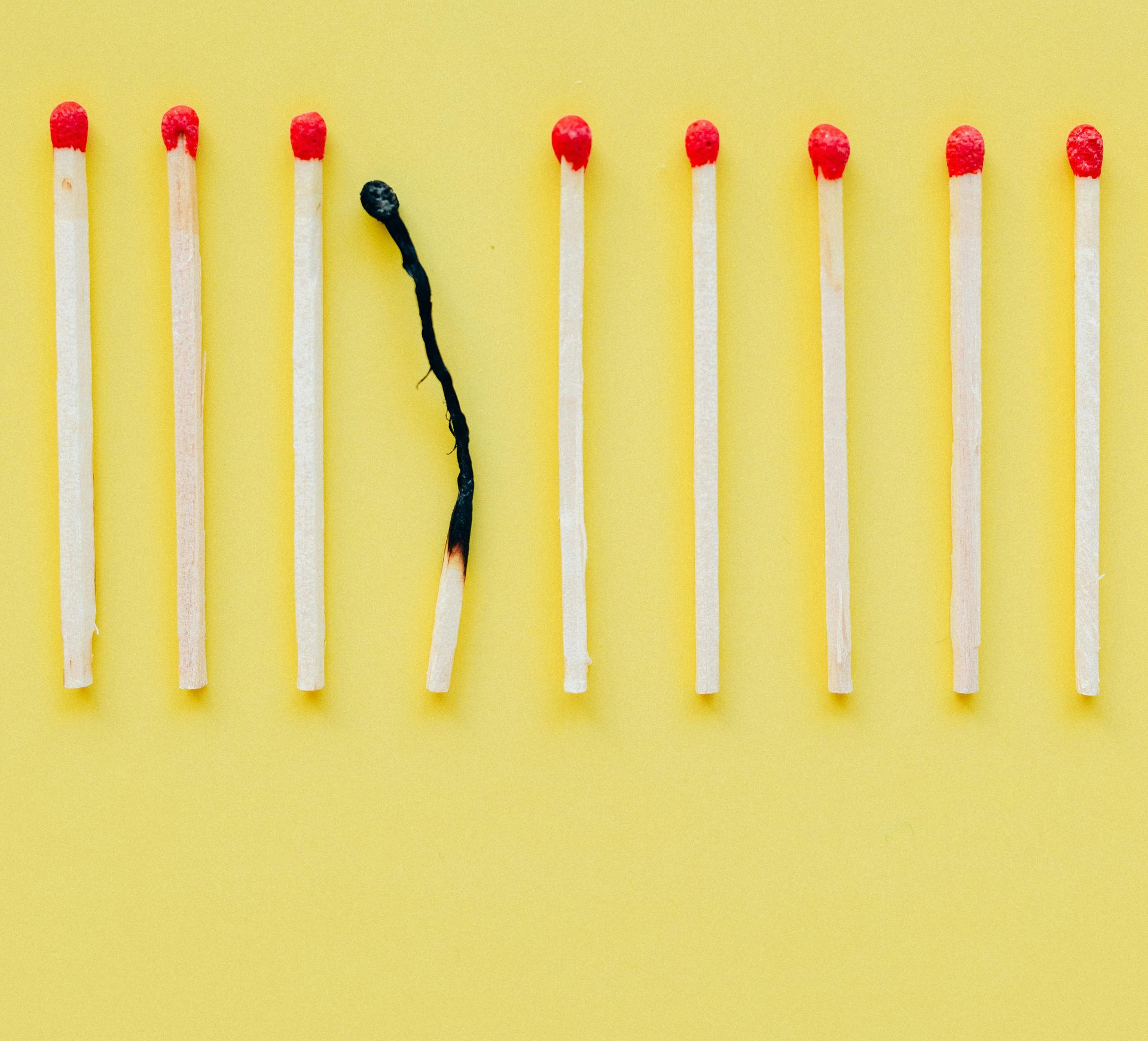 Matches on yellow background, one burned match among others, highlighting burnout.