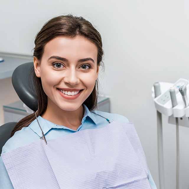 A woman is smiling while sitting in a dental chair.