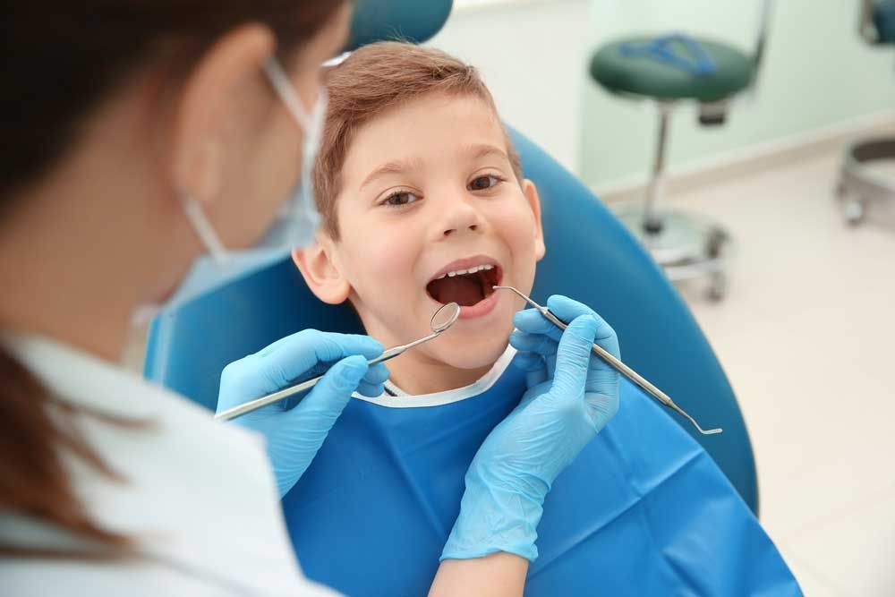 A young boy is sitting in a dental chair while a dentist examines his teeth.