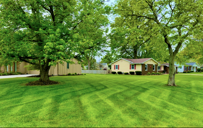 Lush green lawn with patterned mowing, framing houses with trees in the background.