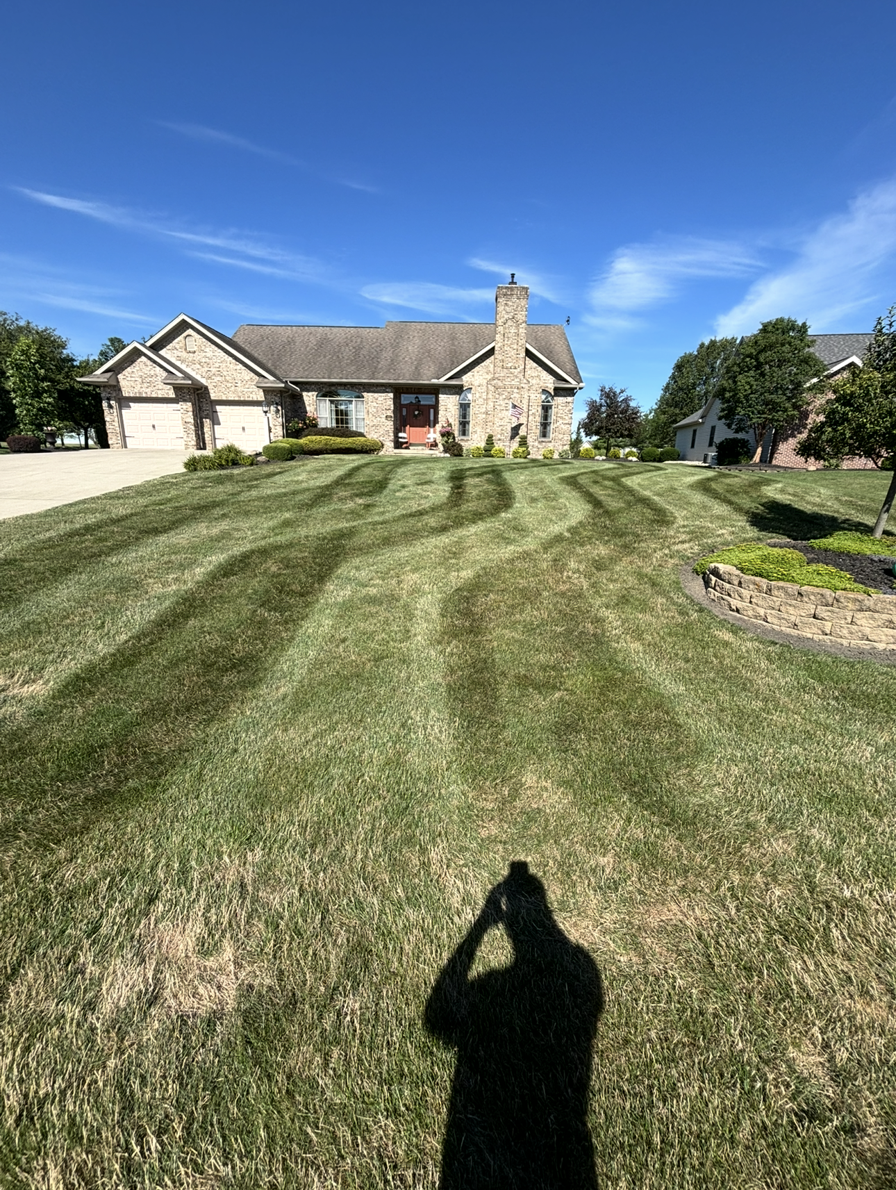 Lawn with striped mowing patterns leading to a brick house under a blue sky,