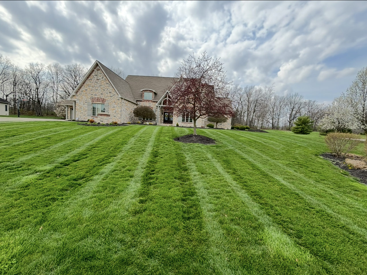 A brick house on a hill with a green lawn mowed in stripes under a cloudy sky.