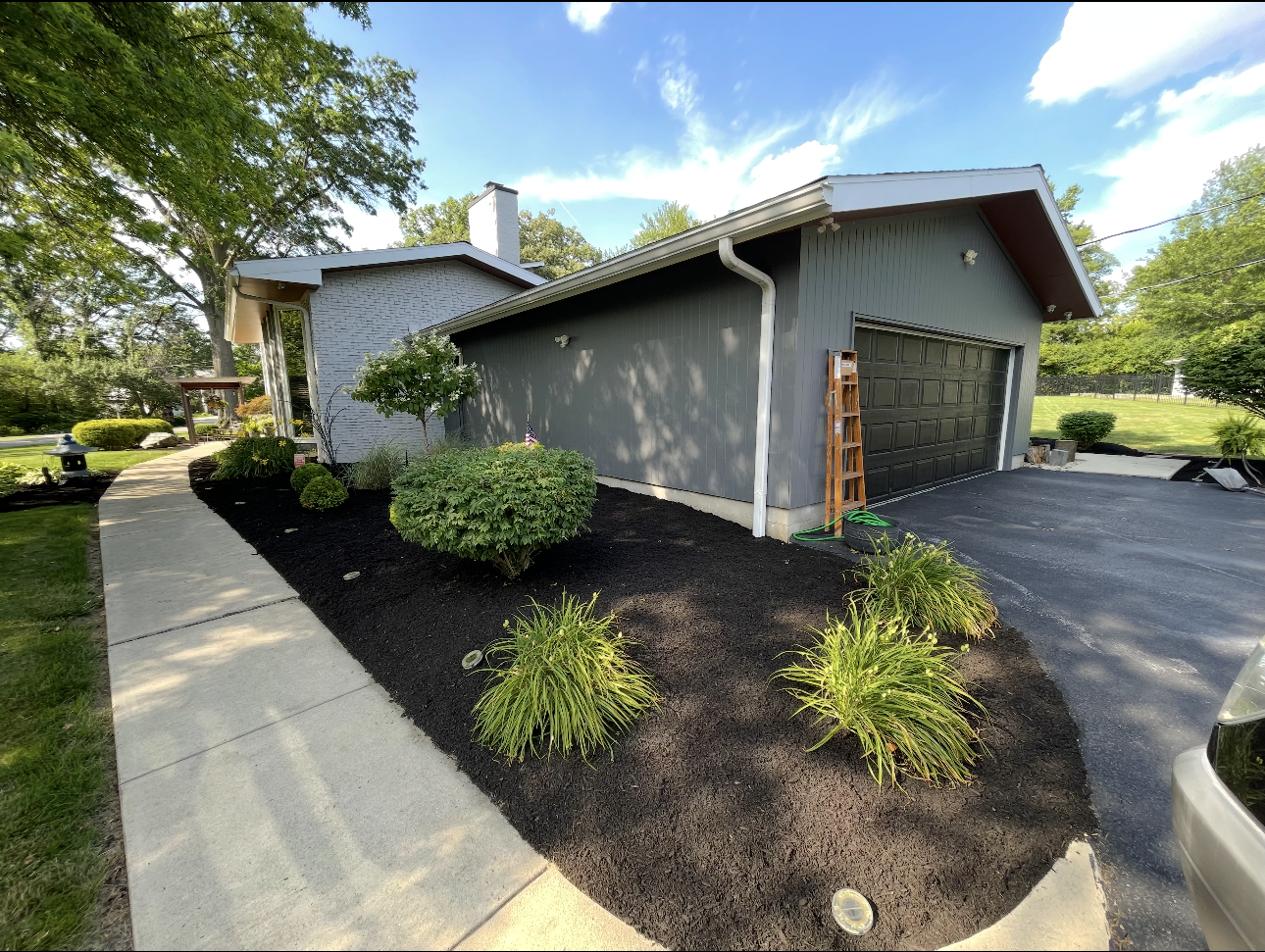 Gray house with black mulch landscaping, shrubs, and a paved driveway.