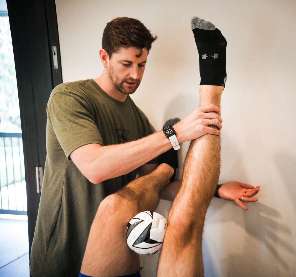 A man in a green shirt is stretching another man 's leg