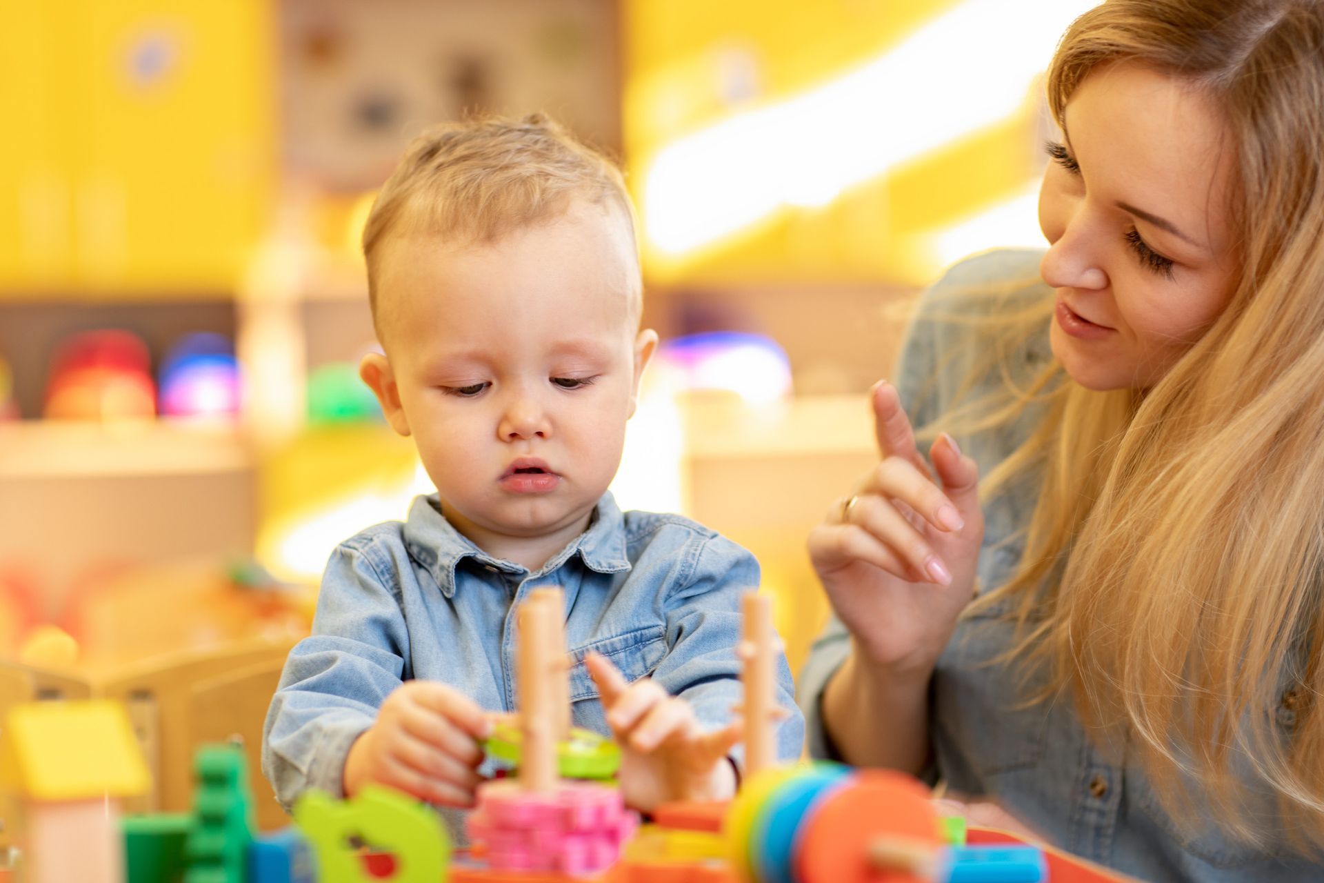 Young child intently plays with colorful stacking rings while a woman watches.