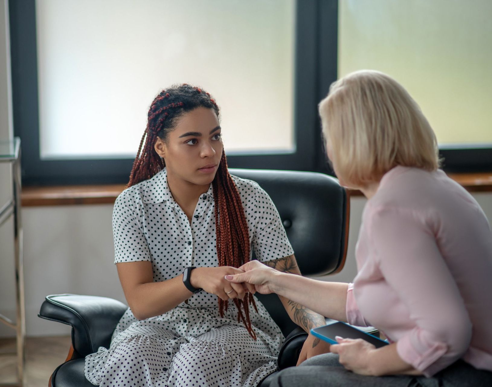 Woman with red braids holding hands with a blond woman in an office setting.