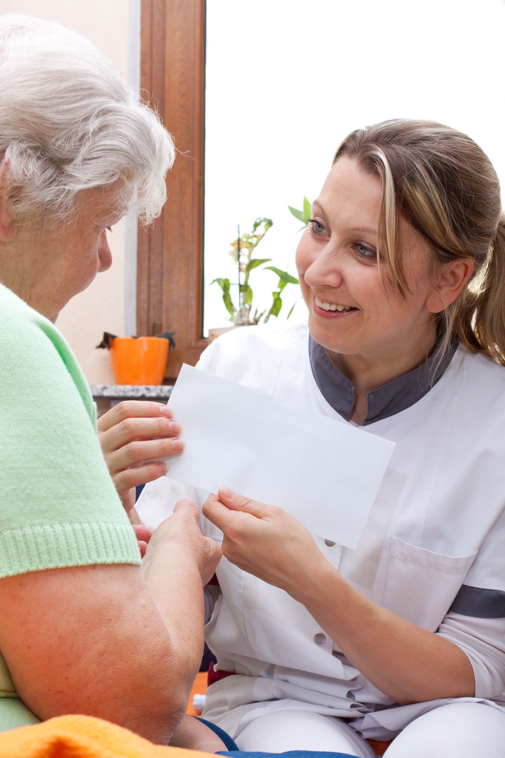 Caregiver showing paperwork to elderly woman, smiling. Light skin, white coat.