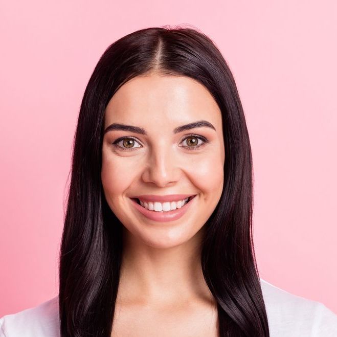 Woman with dark hair smiles at the camera against a pink background.