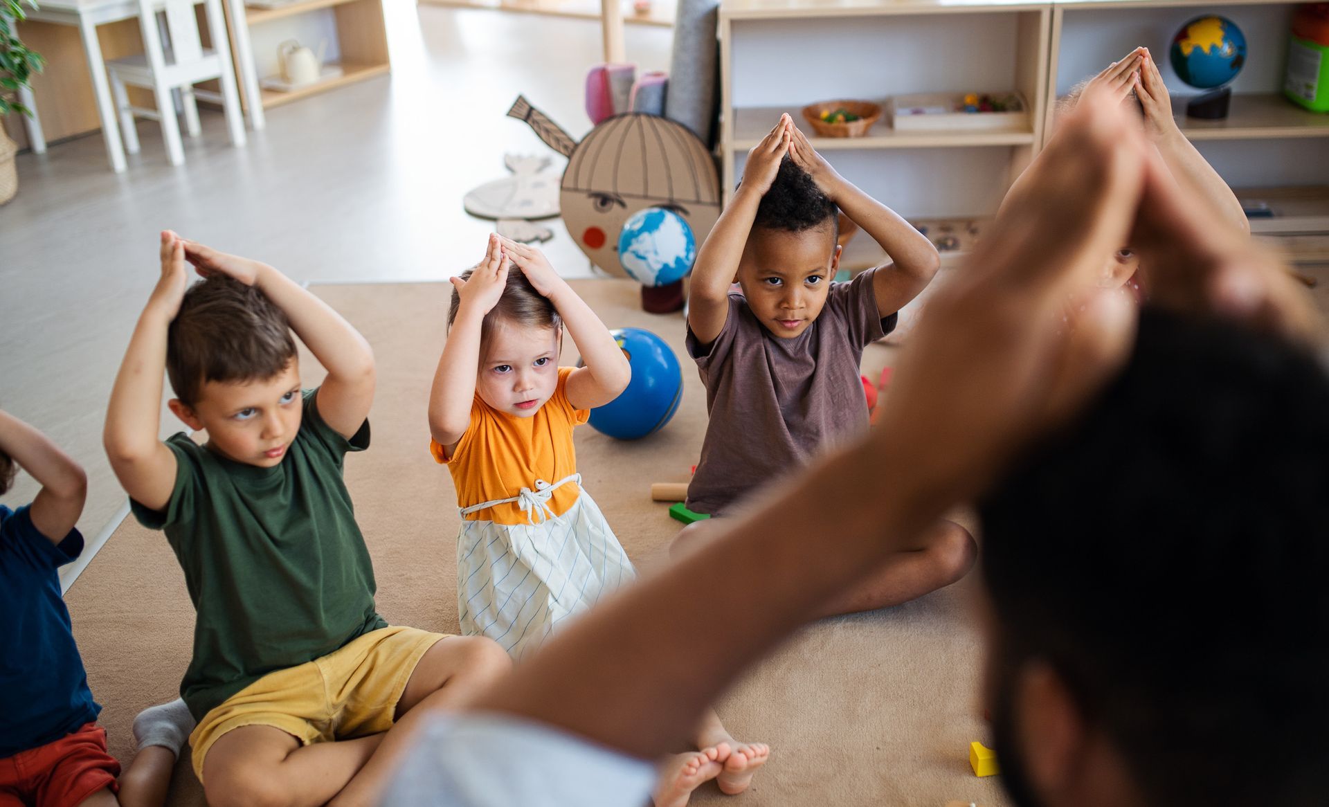 Children and teacher doing a hand yoga pose on the floor indoors.