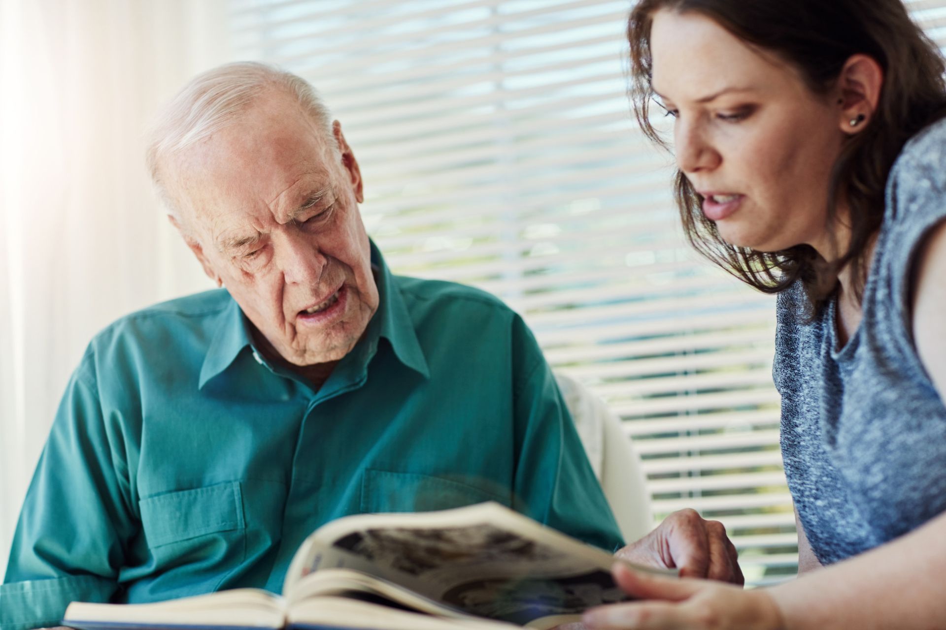An older man and younger woman looking at a photo album, possibly reminiscing together.