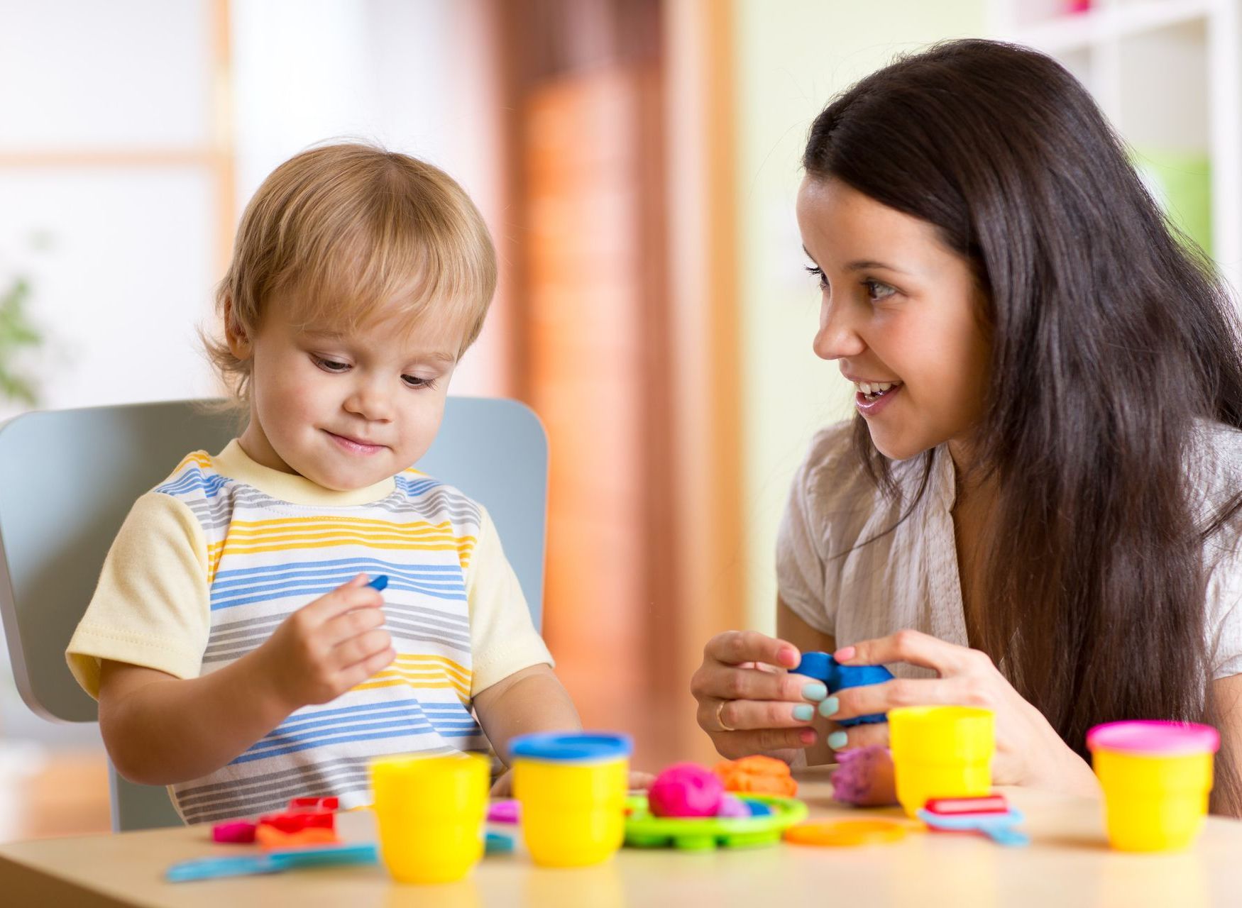 Woman and child playing with colorful playdough at a table.