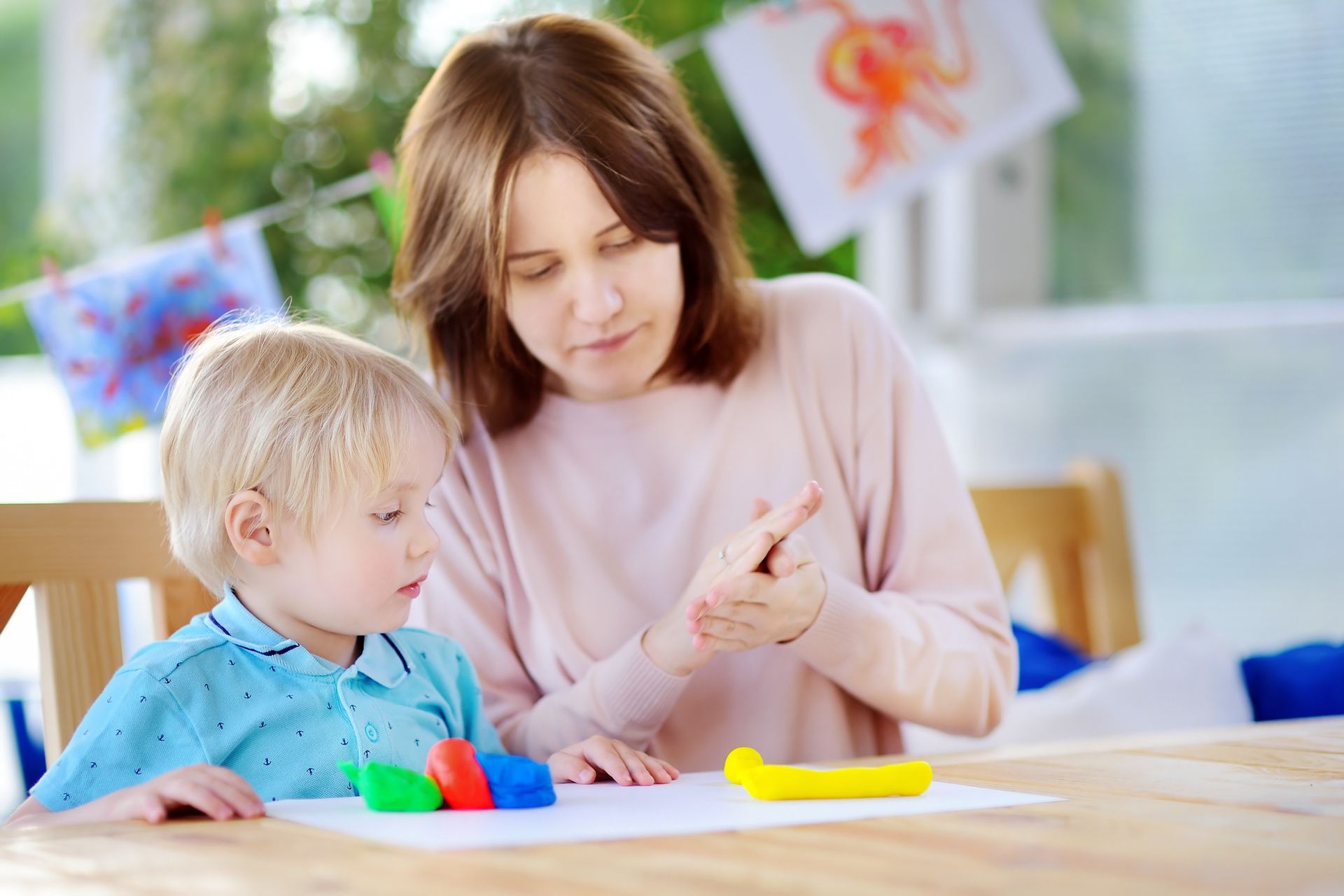 Woman and child playing with colorful clay at a table. Indoors.