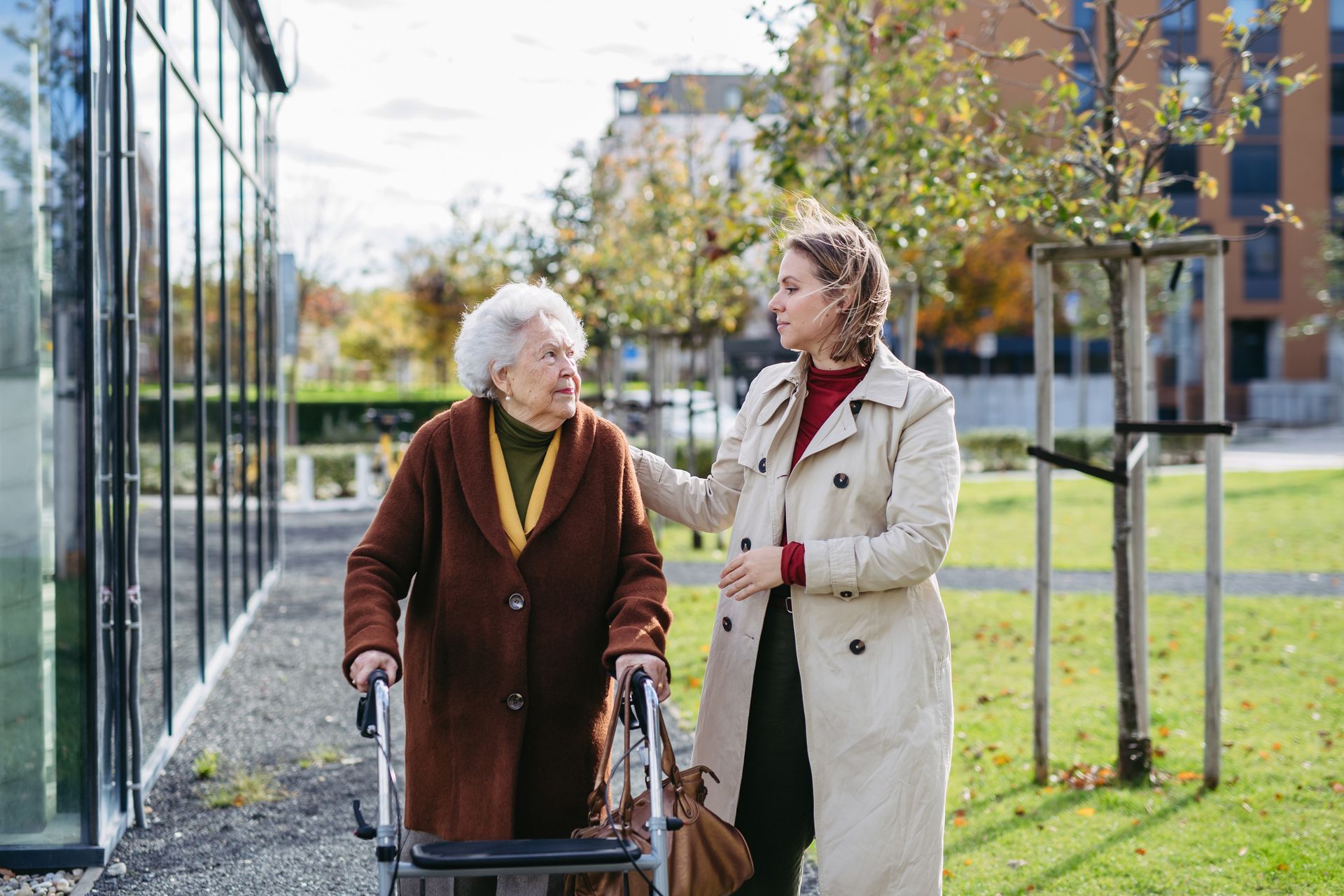 Woman assists elderly woman with a walker outside.
