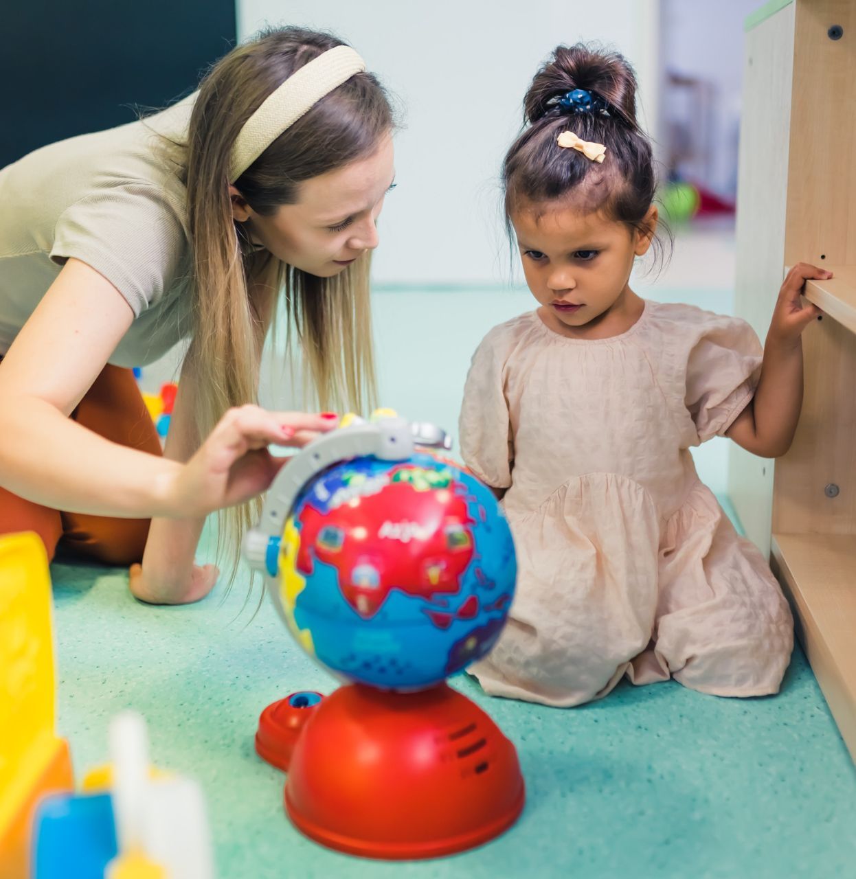 Woman showing a globe to a young girl; both are in a brightly-lit room.