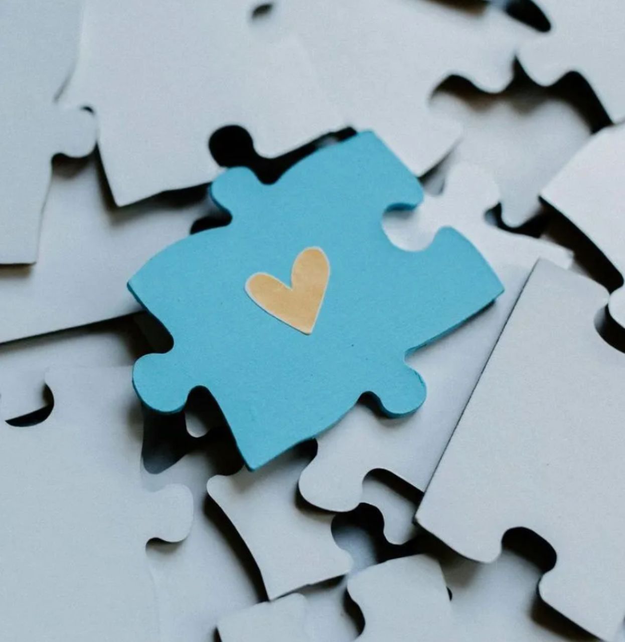 Blue puzzle piece with a golden heart on a pile of grey puzzle pieces.
