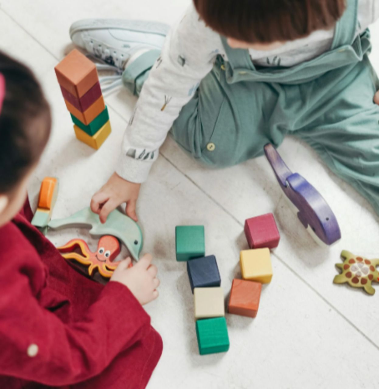 Children playing with wooden blocks and animal toys on a light floor.