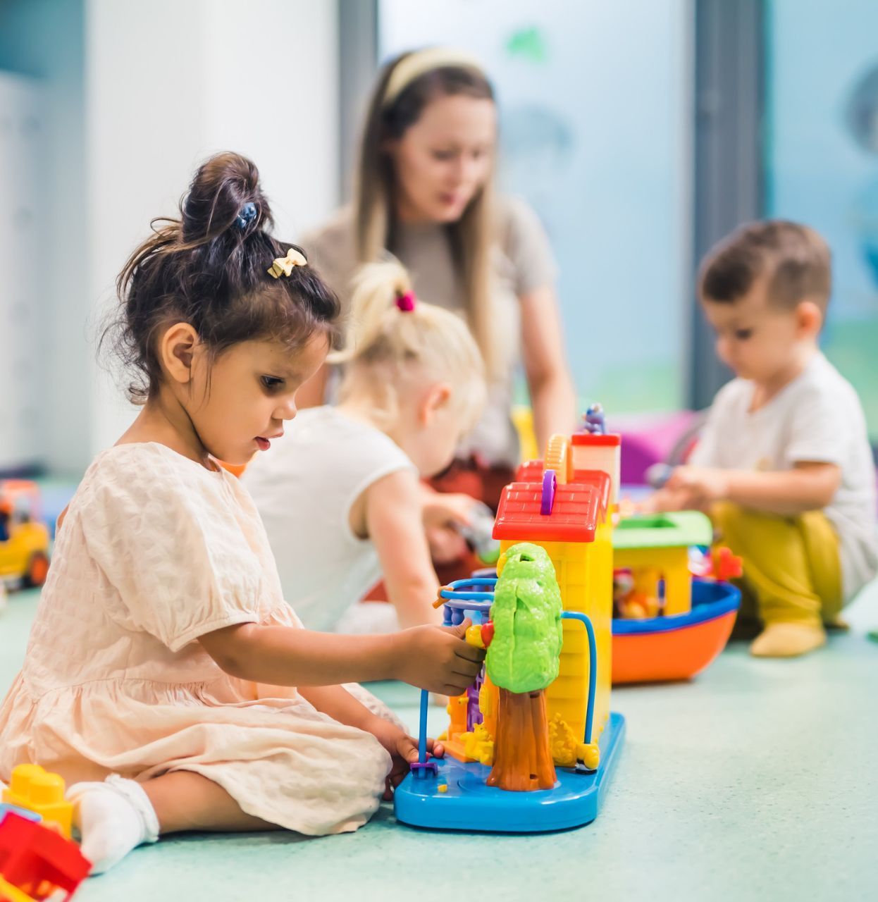 Children playing with toys in a daycare setting. A teacher watches over them.