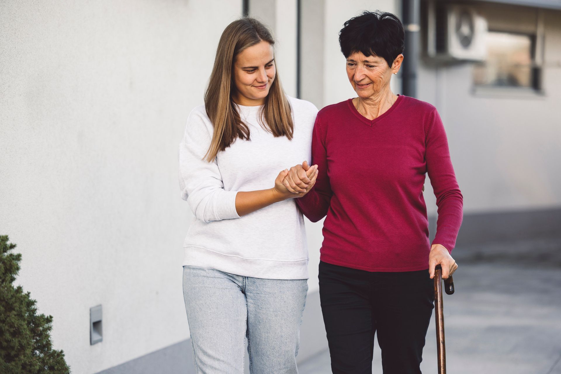Woman in red top helped by younger woman as they walk together, outdoors.