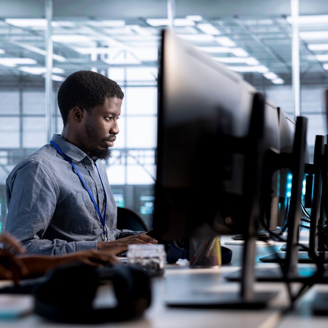 Black man with lanyard works on computer in modern office.