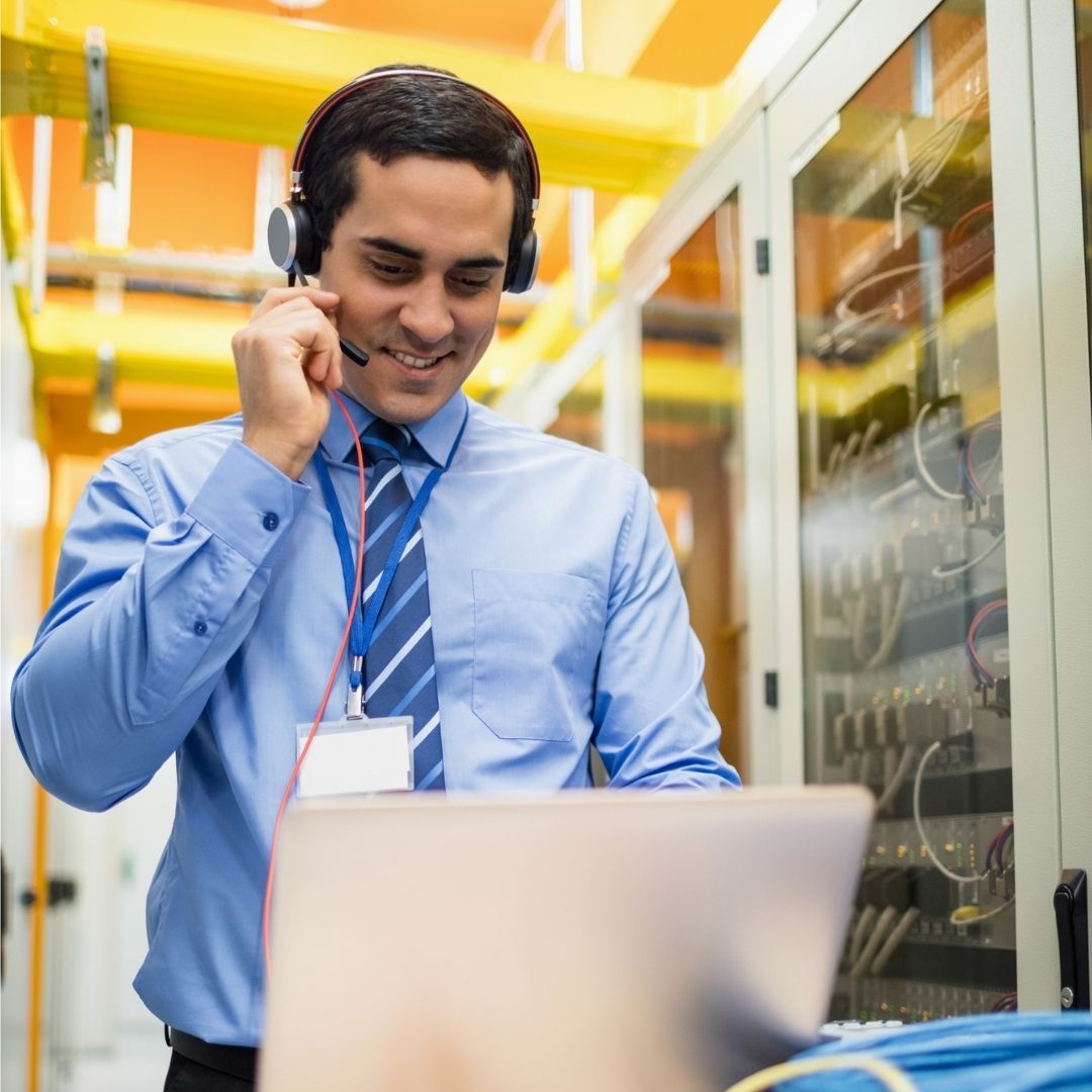 IT support worker in data center, wearing headset and looking at laptop.
