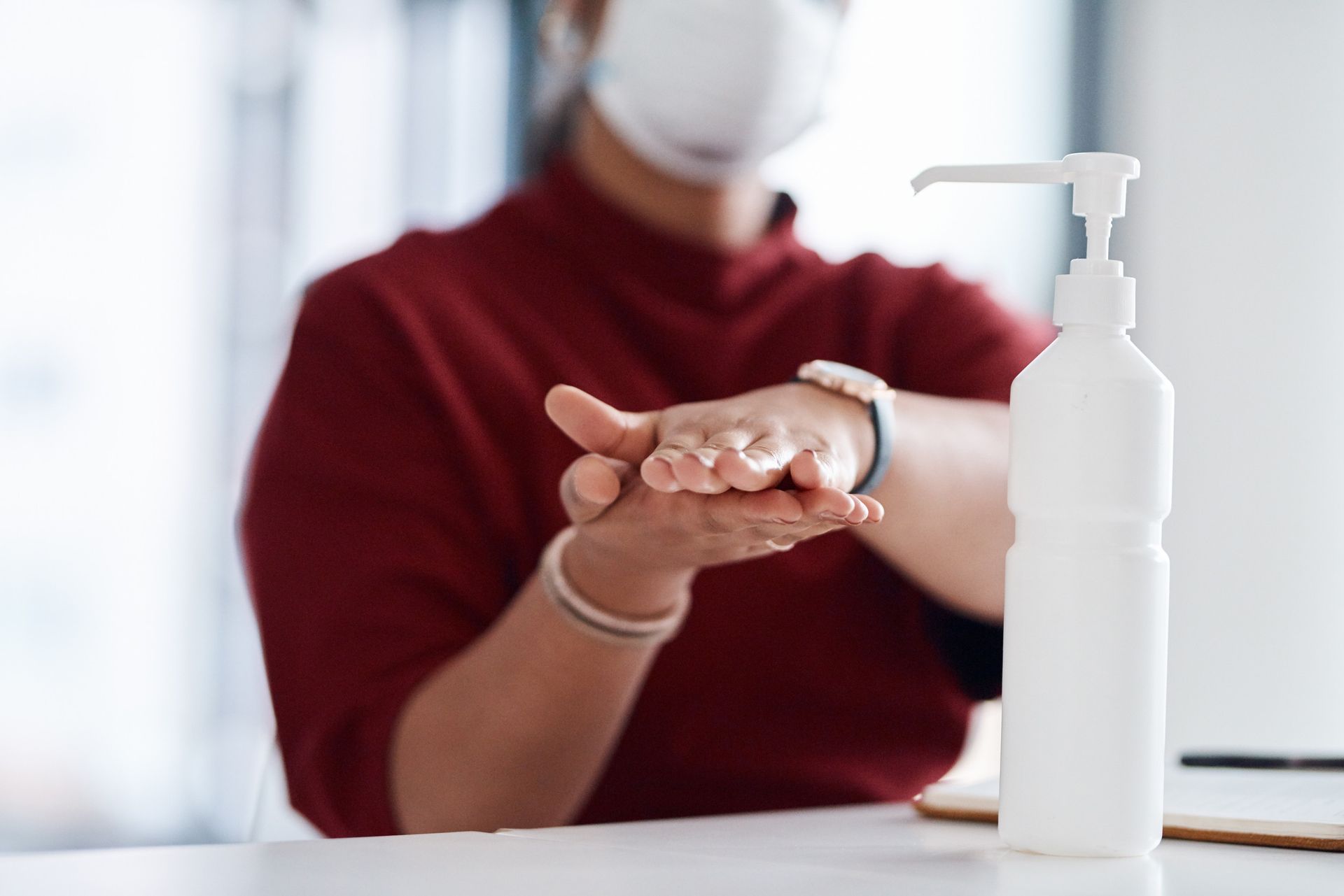 Person in red shirt and mask using hand sanitizer from a white bottle.