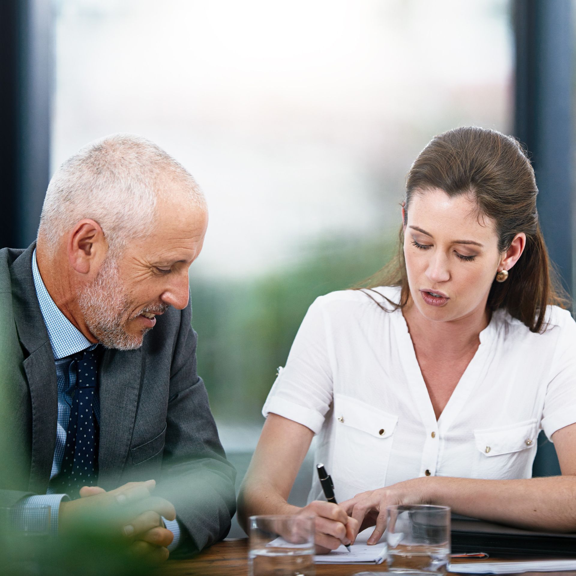 Man and woman in a business meeting, the woman writing, the man looking on.