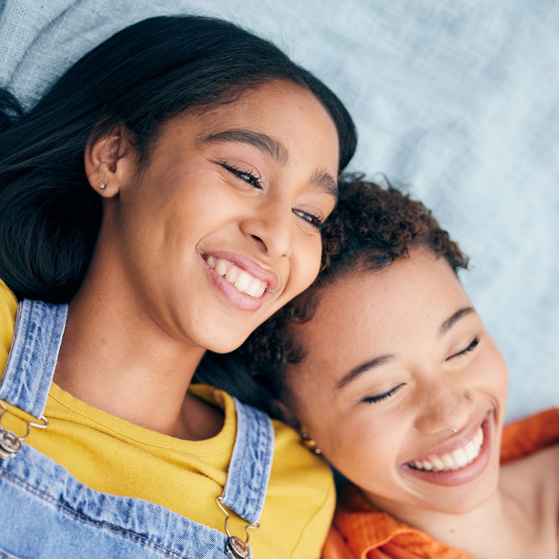 Two smiling young women, one with dark hair, one with short hair, embracing on a blue blanket.