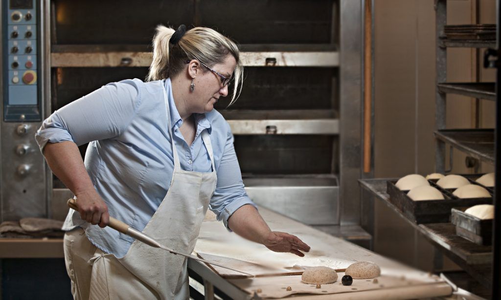 A woman in an apron is cutting dough in a bakery