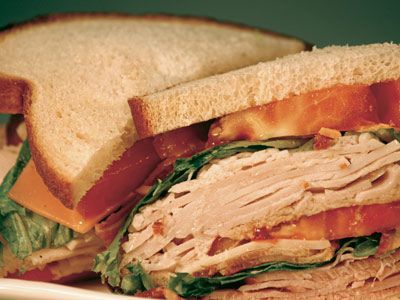 A sandwich with turkey , lettuce , tomatoes and cheese on a plate.