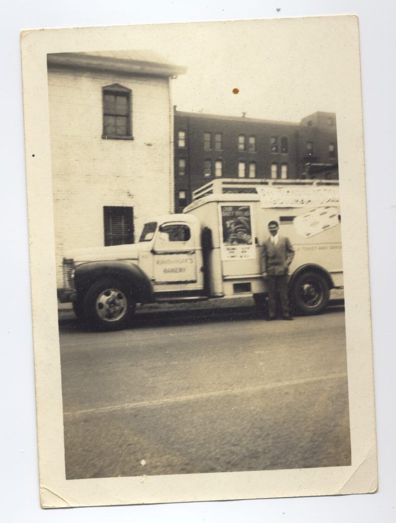 A black and white photo of a man standing next to a white truck