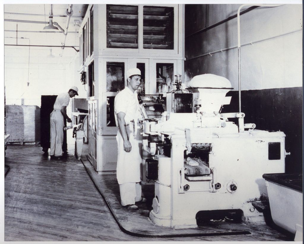 A black and white photo of a man standing in front of a machine