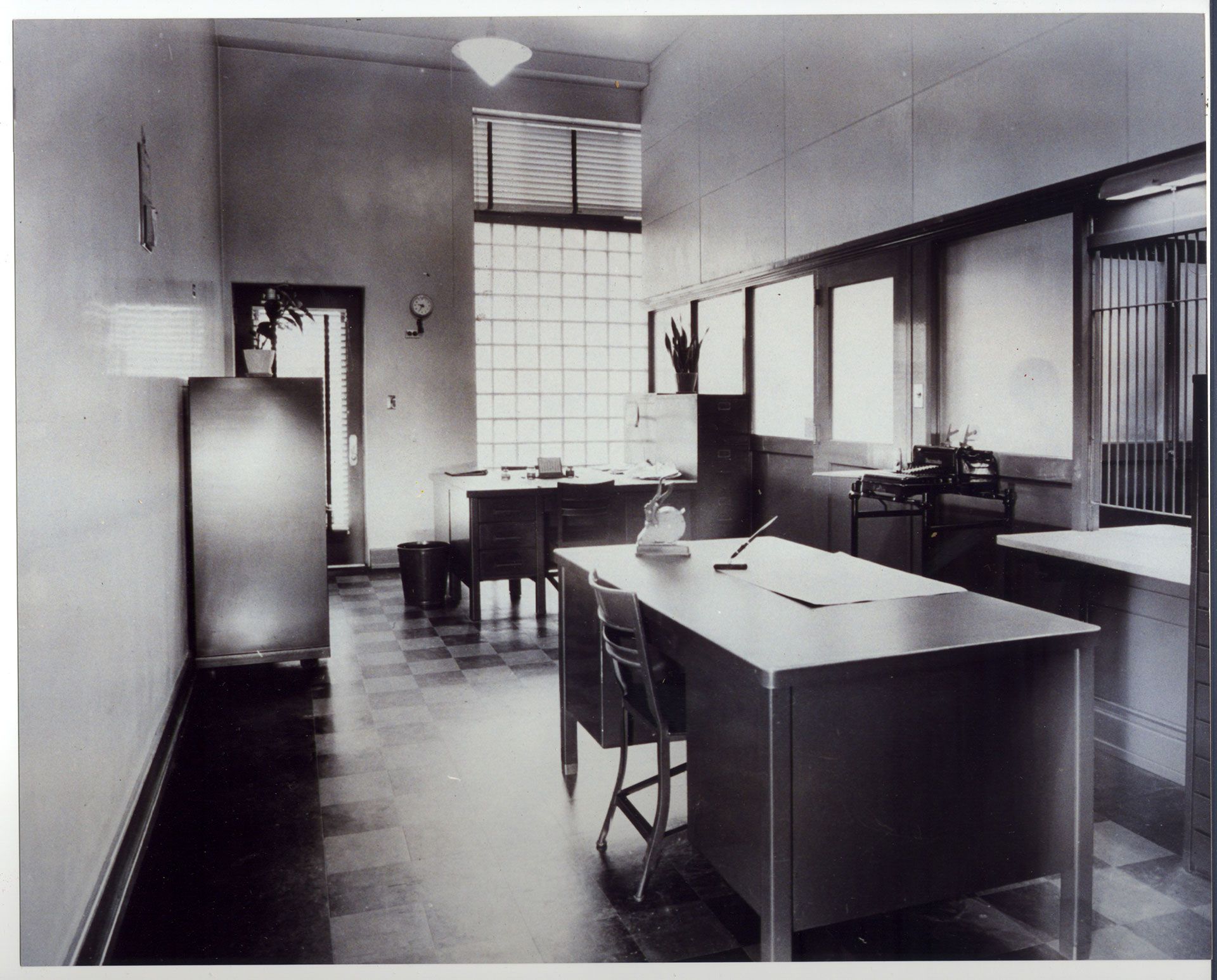 A black and white photo of an office with a desk and chairs