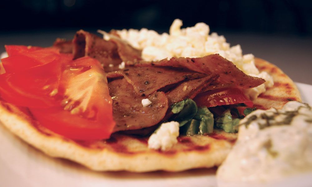 A close up of a gyro with tomatoes and cheese on a plate.