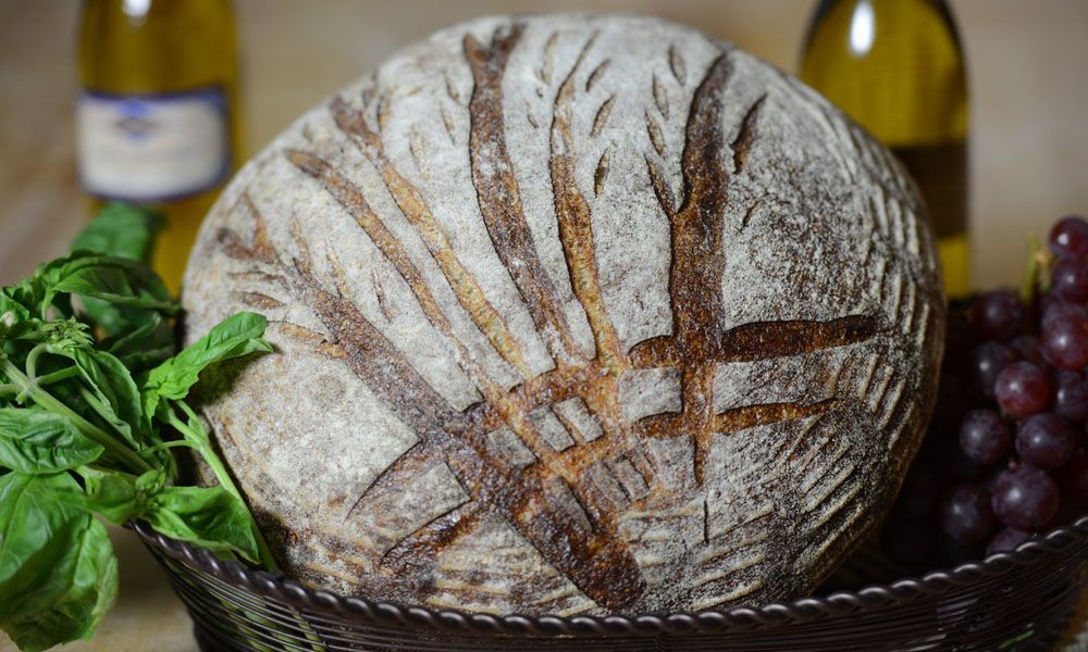 A loaf of bread is sitting in a basket next to grapes and basil.