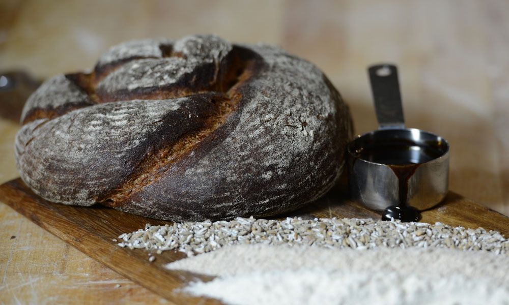 A loaf of bread is sitting on a wooden cutting board next to a measuring cup.