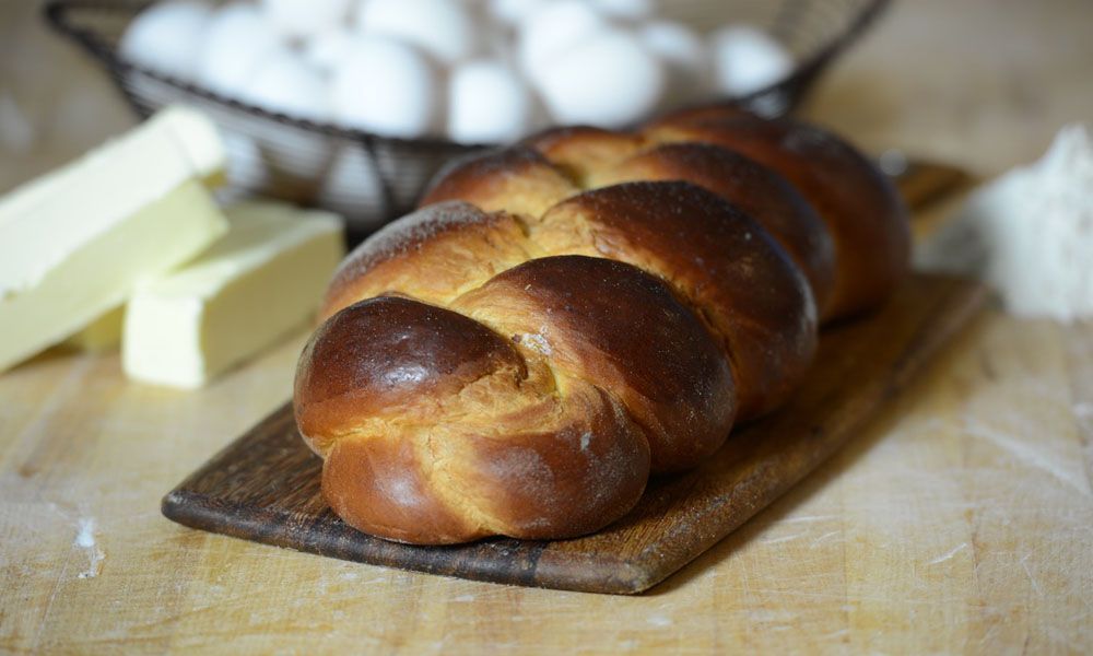 A loaf of challah bread is sitting on a wooden cutting board.