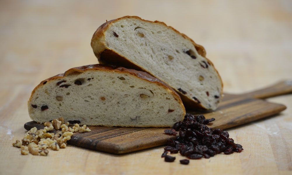 A loaf of bread with raisins and walnuts on a wooden cutting board.