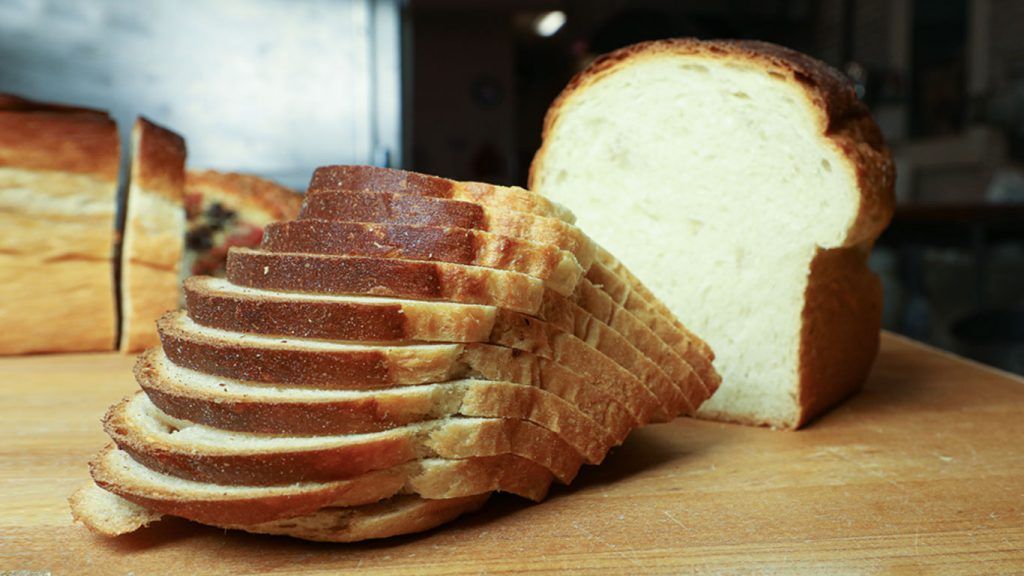 A loaf of bread is sitting on a wooden cutting board next to a sliced loaf of bread.