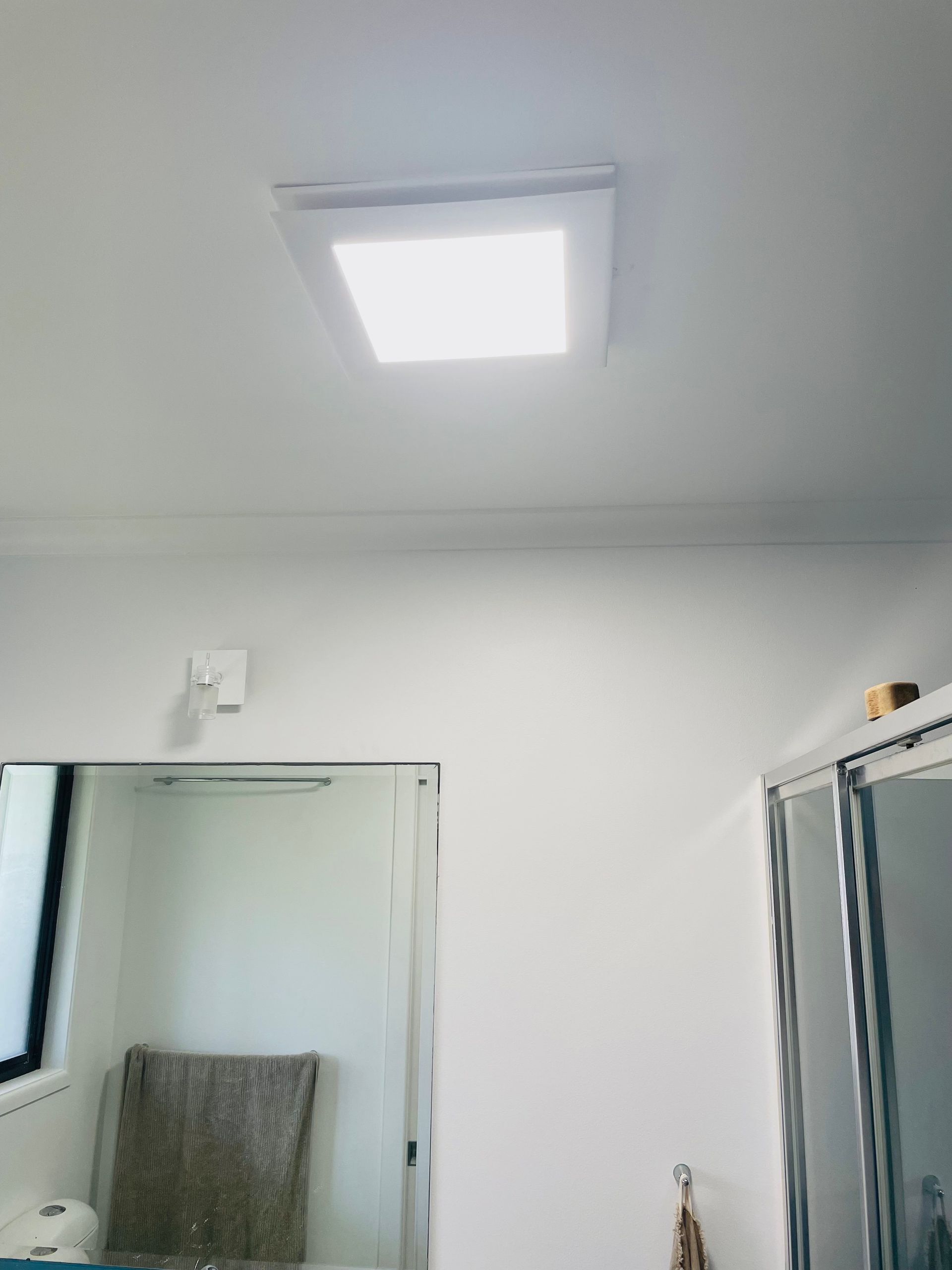 Square recessed ceiling light illuminating a white room. A mirror and shower door are visible.  — Grant Murphy Electrical in Kingscliff, NSW