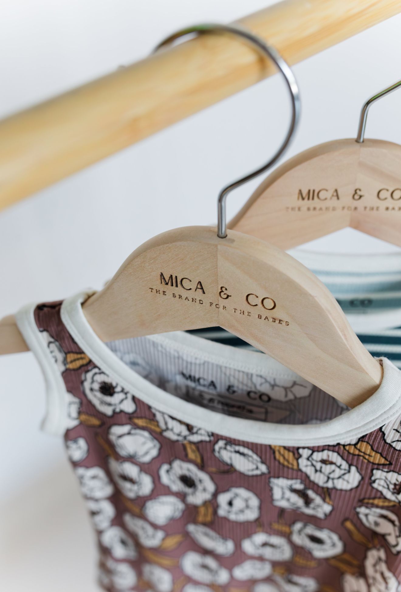 Two wooden hangers displaying children's clothes. The hangers are branded