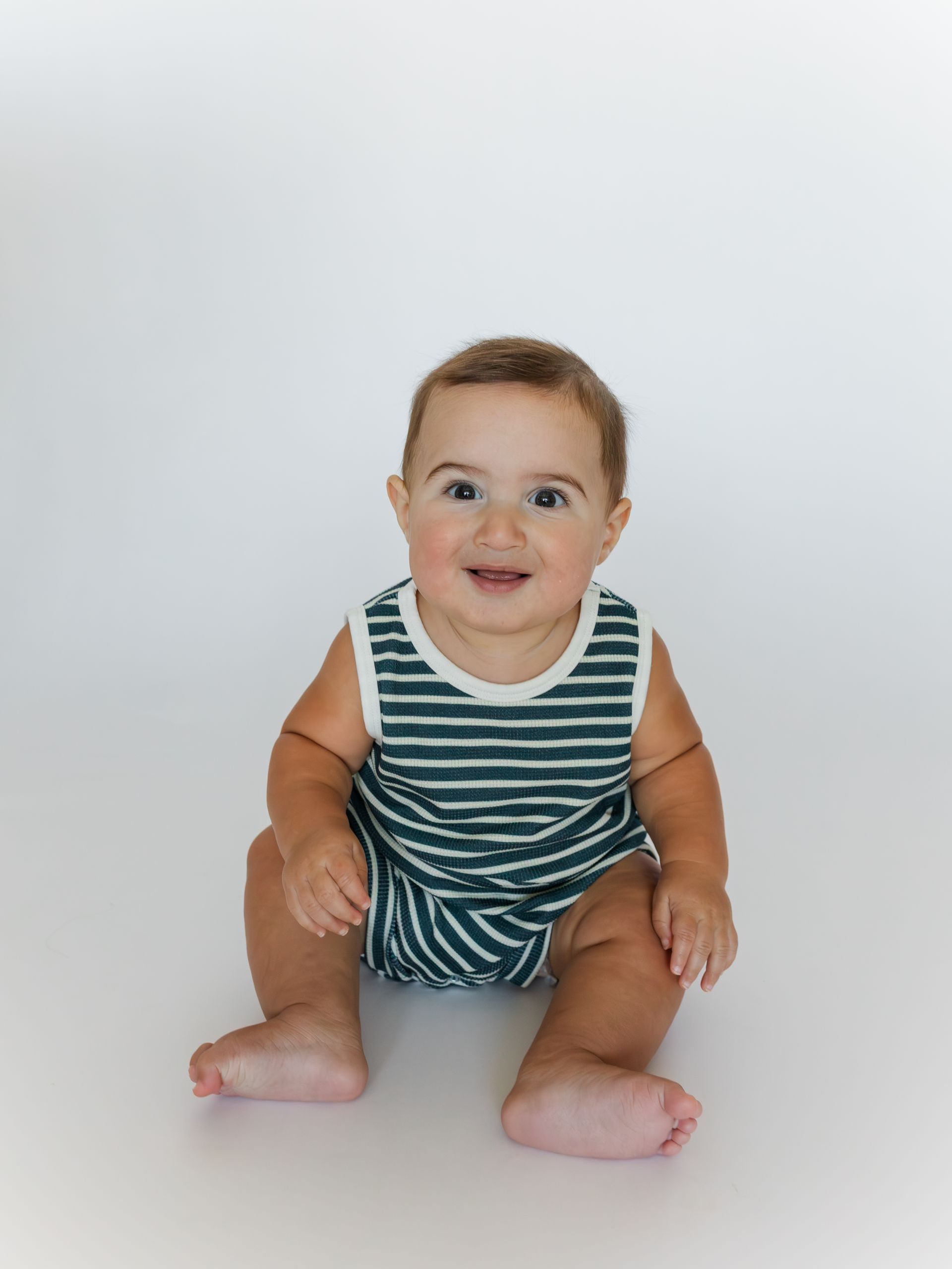 Smiling baby, seated, in a green striped onesie against a white background.