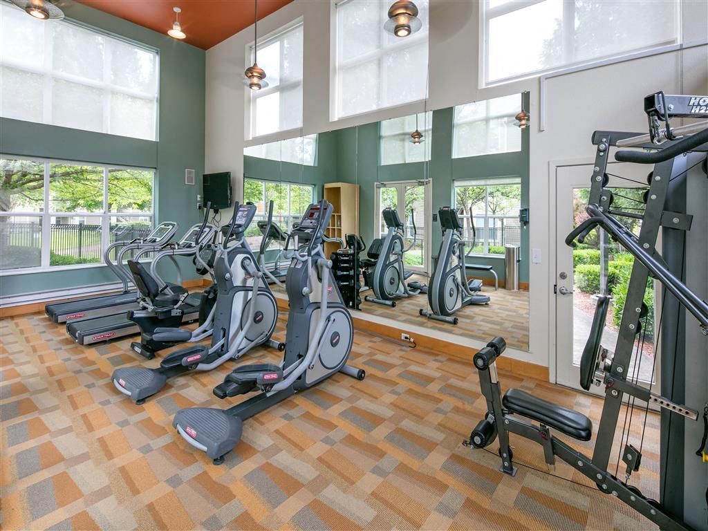 Bright fitness center with treadmills, ellipticals, and weight machines reflected in mirrors.